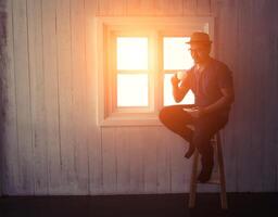 hombre guapo bebiendo café o té cerca de la ventana sentado en la silla de madera de su habitación foto