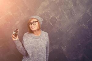 mujer hipster sonriente con gafas sosteniendo una cámara retro con fondo beige foto