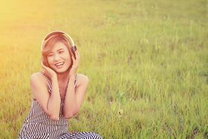 Beautiful sexy woman sitting  listening music from headphone smiley enjoying music in the grass field photo