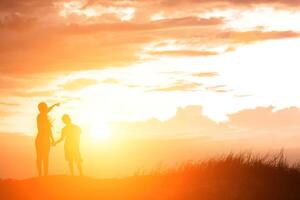 silhouette mother and son at sunset , pointing at the sun photo