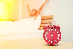 hermosa joven se despierta estirada en la cama por la mañana con un reloj despertador que se ve tan fresca foto