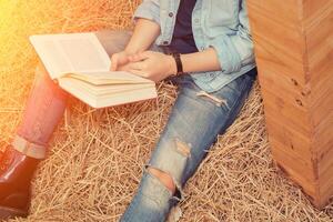 young man reading book and sitting on straw in the farm photo