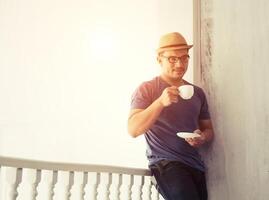 un hombre guapo que se encuentra fuera de casa se apoya en el balcón tomando café por la mañana foto