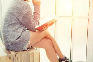 mujer joven leyendo un libro, de cerca, en el fondo interior de la casa cerca de la ventana foto