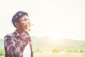 hombre hipster fumando cigarrillo, parado detrás de una montaña. entre el aire fresco de la mañana. foto