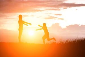Mother encouraged her son outdoors at sunset, silhouette concept photo
