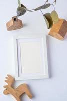 marco de fotos con rama de eucalipto en jarrón de madera y juguete de madera sobre fondo blanco