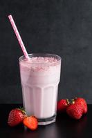 Milkshake with strawberries on black background. Summer drink in a glass with a paper straw. photo