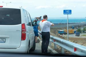 taman, rusia-19 de mayo de 2018- un hombre con una corbata pionera roja se para en el auto y fotografía el puente de crimea. foto