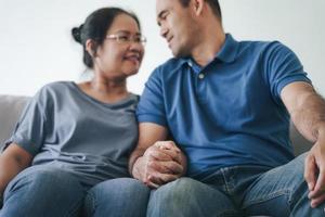 Portrait of Asian mature couple sitting in the living room. wife and husband hugging, holding hand with happiness and cheerful. Love, safety, and insurance family concept photo