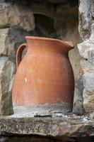 Ancient handmade clay wine jug with spider web standing on a stone window in the middle of stone wall. Decoration and craft for background.
