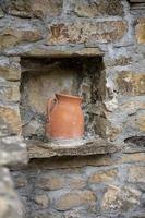 Ancient handmade clay wine jug with spider web standing on a stone window in the middle of stone wall. Decoration and craft for background.