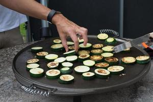 Grilling sliced zucchini. Hands of two unrecognizable women taking care of them photo