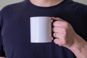 Man holding a white cup of hot beverage outdoors. photo