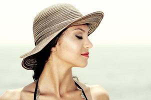 Attractive woman with a sun hat on a tropical beach, eyes closed photo