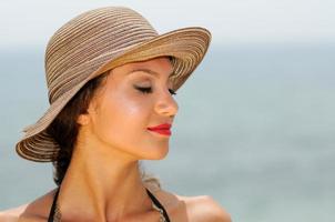 Attractive woman with a sun hat on a tropical beach, eyes closed photo