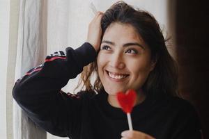 mujer latina enamorada de una piruleta en la mano en forma de corazón. día de San Valentín foto