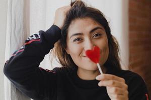 mujer latina enamorada de una piruleta en la mano en forma de corazón. día de San Valentín foto