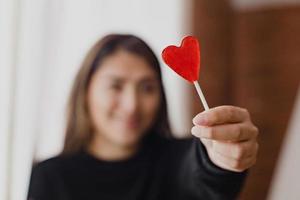 mujer latina enamorada de una piruleta en la mano en forma de corazón. día de San Valentín foto