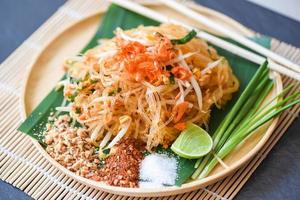 Thai food fried noodle Thai style with prawns bean sprout and garnish peanuts chili powder sugar lemon lime, Stir-fry noodle Pad Thai on plate served on the dining table food - top view photo