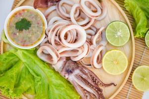 squid rings on wooden plate, Fresh squid cooked boiled with lettuce vegetable salad lemon and seafood sauce on table background photo