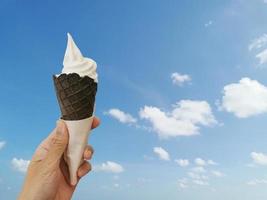 Delicious ice cream in waffle cone in female hand with blue sky background for summer season. Summer and vacation concept. photo