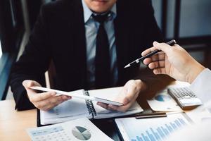 Two business people using digital tablets to analyzing reports of business operating expenses together to summarize note summary information in the office. photo