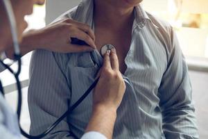 el médico asiático está usando un estetoscopio para escuchar los latidos del corazón del paciente anciano. foto