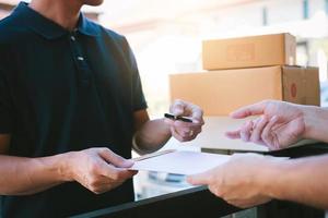 Young asian man smiling while delivering a cardboard box to the woman holding document to signing signature. photo