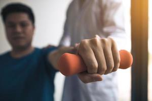 Asian physiotherapist helping a patient lifting dumbbells work through his recovery with weights in clinic room. photo