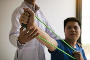 cierre el paciente de la mano haciendo ejercicio de estiramiento con una banda de ejercicio flexible y una mano de fisioterapeuta para ayudar en la sala de la clínica. foto