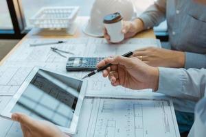 Two engineering working together and using digital tablet looking blueprint and analysis with architectural plan on desk. photo