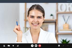 Smiling young Caucasian woman in white blazer sitting in living room looking at camera while making video call, online interview and work from home concepts photo