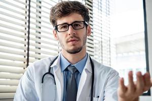 Young male doctor looking at camera explaining and talking with patient online via video calling, distance medical consulting service and telehealth concepts photo