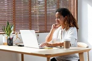 Young happy African-American woman using laptop computer working from home in the time of pandemic photo