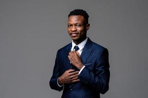 retrato de un joven africano apuesto que usa traje de negocios formal con corbata y mira la cámara aislada en el fondo gris del estudio foto