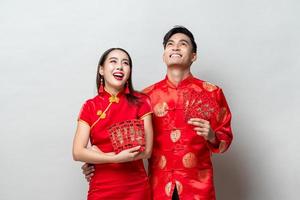 pareja asiática con trajes orientales tradicionales sosteniendo sobres rojos o ang pow en fondo gris para conceptos de año nuevo chino, textos extranjeros significan gran suerte, gran beneficio y todo va bien foto