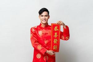 Handsome smiling Asian man showing red scroll  in isolated studio light gray background for Chinese new year concepts, foreign text means may you attain greater wealth photo