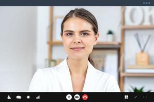 Smiling young Caucasian woman in white formal suit looking at camera while making video call, distance meeting and work from home concepts photo