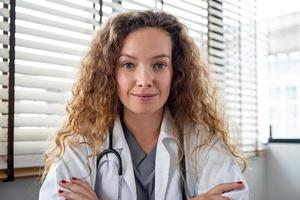 Smiling female doctor looking at the camera while making online video call, home medical consulation service concepts photo