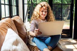 Pretty smiling Caucasian woman using laptop computer on the couch at home