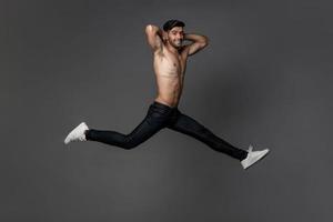 un apuesto hombre caucásico sonriente sin camisa saltando con las piernas abiertas de par en par en un fondo gris de estudio aislado foto