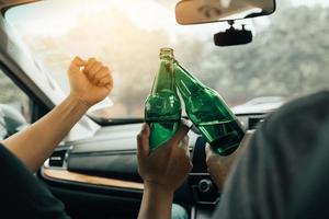 dos amigos varones están celebrando en el auto mientras tocan una botella de cerveza juntos. foto