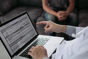 Doctor is using a laptop while typing the patient personal history record and giving advice about the patient home treatment. photo