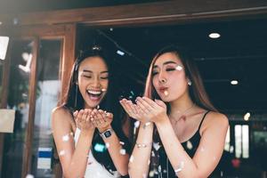 Two asian women blowing paper confetti for a celebration in his home. photo