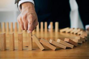 Close up finger businessman stopping wooden block from falling in the line of domino with risk concept. photo