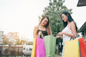 Beautiful asian female friends standing and looking in paper bag at outdoors shopping mall center retail in the city. photo