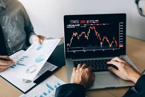 Two investors are working together with analyzing the stock data graphs in the paper and viewing the data on the laptop screen. photo