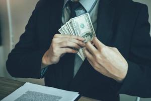 Businessman putting stack of money bills in his suit coat pocket. photo