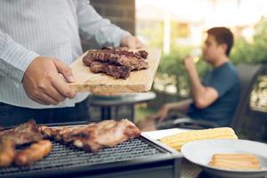 los hombres asiáticos están preparando carne de cerdo que se coloca en una tabla de cortar de madera y se la llevan a los amigos que están celebrando en la parte de atrás. foto